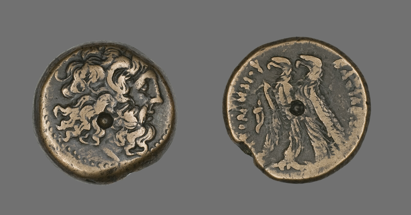 Both sides of a bronze Ptolemaic coin, one with the bearded head of Zeus, one with two eagles.